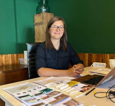 Zu sehen ist Eszter Csépe-Bannert, die vor einem ausgeklappten Laptop an einem Schreibtisch sitzt.