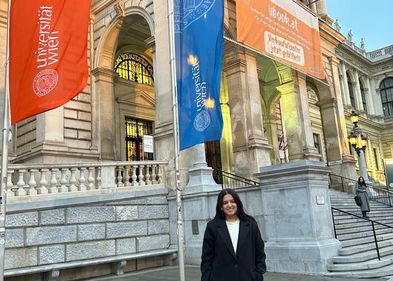 Kanishka steht vor dem Eingang eines der Gebäude der Universität Wien.