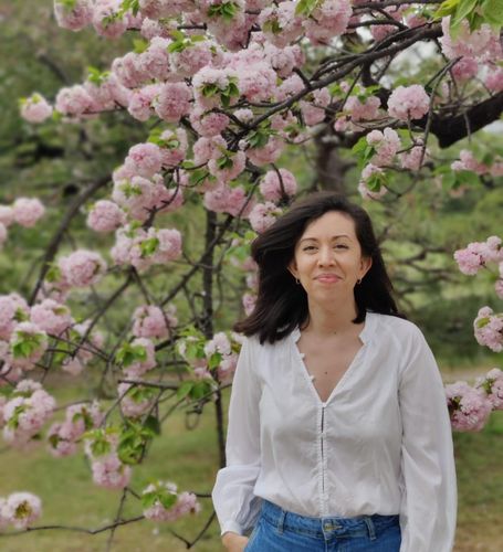 A woman with long, black hair standing in front of a blooming tree.